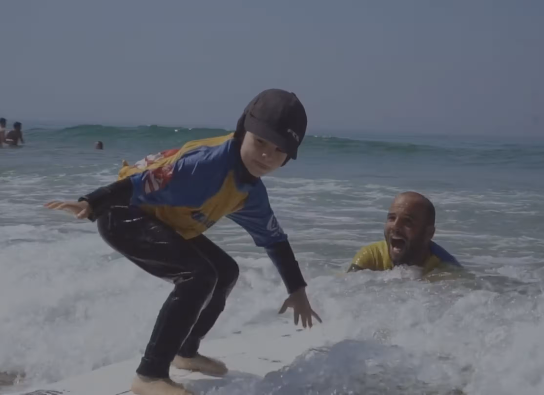 Child surfing a small wave with a Surf Lisbon instructor during a kids surf camp in Lisbon.