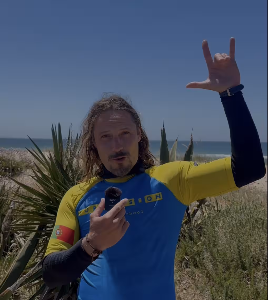 SurfLisbon instructor holding a mic during an interview with Caparica beach in the background.
